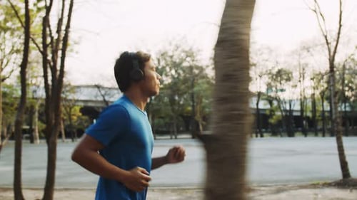Asian man running in the park and listens to music during a beautiful sunset.