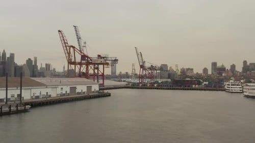 Flying Towards Industrial Cranes in Docks with New York City Skyline in Background and River