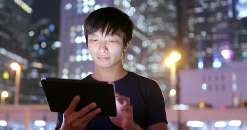 Young Adult Using Tablet Device in City at Night