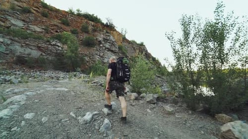 Man Walks With Backpack on Rocky Path by Lake