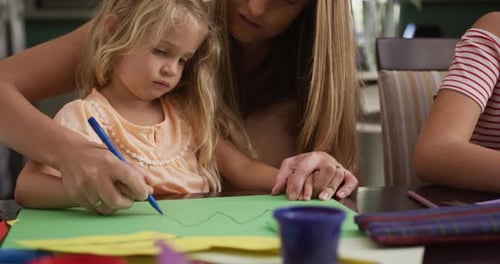 Woman Helps Child Drawing at Table