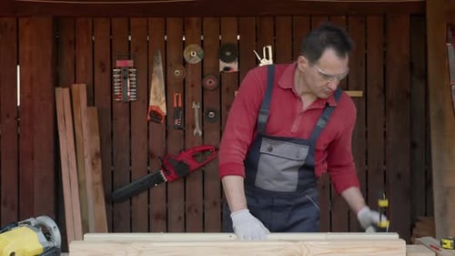 Carpenter Holds Two Wooden Beams in Hands and Compares Their Sizes