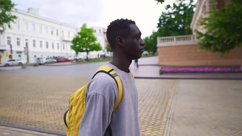 Hübscher junger Afroamerikaner, der mit gelbem Rucksack auf den Schultern in der Stadt spaziert, lässig