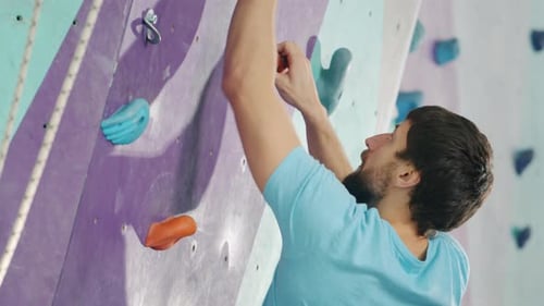 Attractive Bearded Guy Climbing Up the Wall in Rock-climbing Gym Enjoying Activity