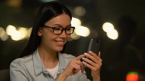 Asiatische Frau scrollt Fotos auf dem Handy, Kommunizieren im sozialen Netzwerk
