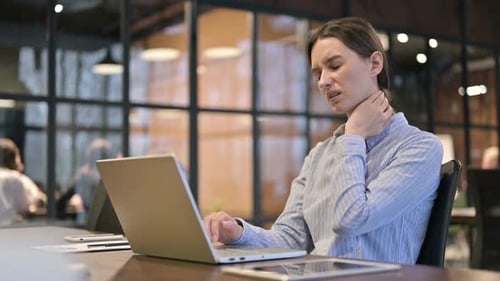 Woman Massaging Neck at Desk in Modern Office