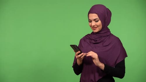 A Young Beautiful Muslim Woman Takes Selfies with a Smartphone Green Screen Background