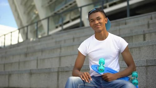 Smiling Teenager Sitting with Skateboard on Urban Steps