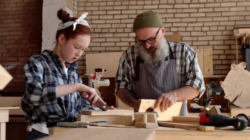 Man and Girl Sanding Wood in Workshop