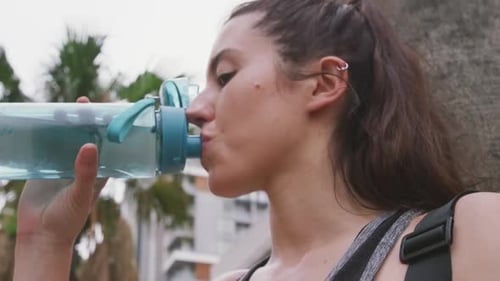 Woman Drinking Water and Using Smartphone Outdoors