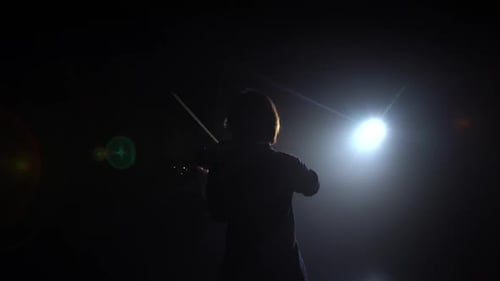 Silhouette of Violinist Performing in Dark Setting