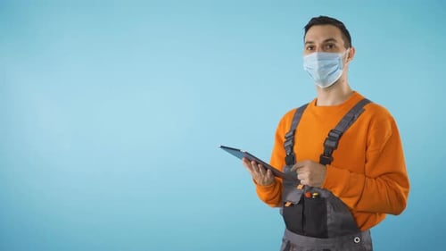 Repairman with Face Mask Working on Tablet Isolated in Studio Blue Background