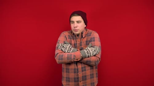 A Young Man in a Red Shirt, Hat and Mittens Is Cold and Hugs Himself To Keep Warm. Shooting in the