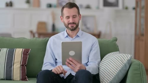 Man On Sofa Uses Tablet For Video Call