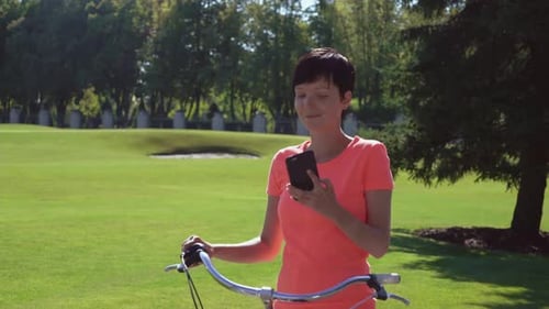 Woman Uses Phone While Holding a Bicycle