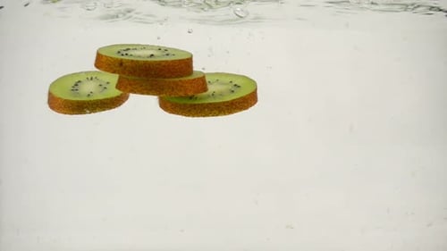 Fruit Slices of Kiwi Slowly Sink Into the Water on a White Background Close-up