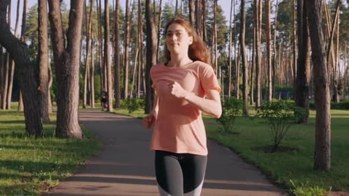 Woman Jogging on Paved Path in Sunny Park
