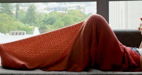 Woman Lying on Sofa Reading Smartphone Under Blanket