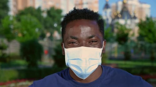 Nahaufnahme: Lächelnder afroamerikanischer Mann mit schützender medizinischer Gesichtsmaske blickt in die Kamera