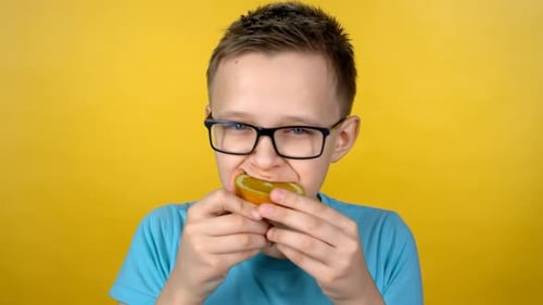 Boy Eats Orange Slice Against Yellow Backdrop