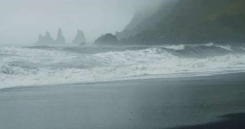 The Black Sand Beach of Reynisfjara with Waves Hitting the Shore on Foggy Rainy Stormy Day