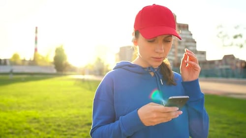 Woman with Wireless Headphones and Smartphone Chooses Music and Runs Through the Stadium at Sunset