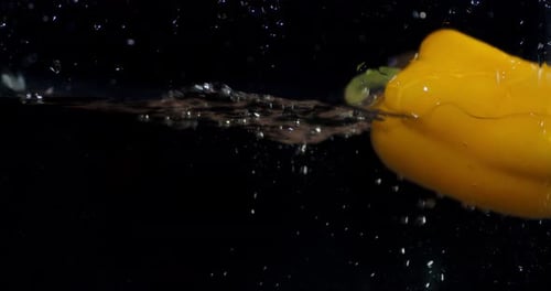 Gelbe Paprika, die mit Spritzern unter Wasser fällt.