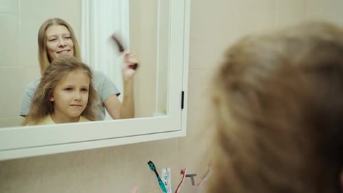 Mother Brushing Daughter's Hair in Bathroom Mirror
