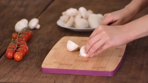 Hands slicing mushroom on wooden cutting board