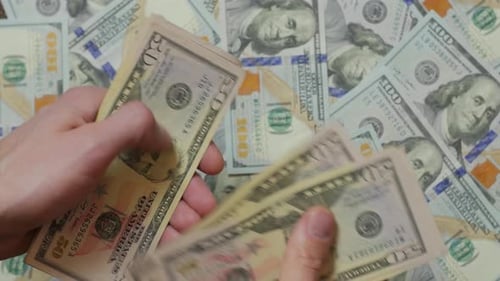 Hands Counting Fifty Dollar Bills over Hundred Dollar Bills