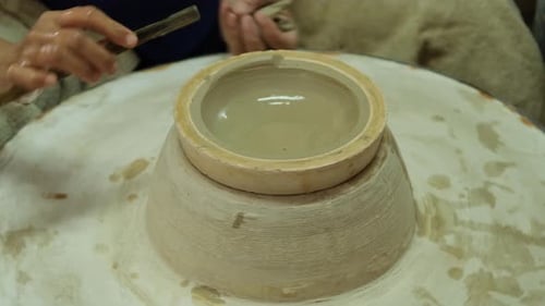 Close-up of a woman working on a potter's wheel making clay objects in pottery workshop.