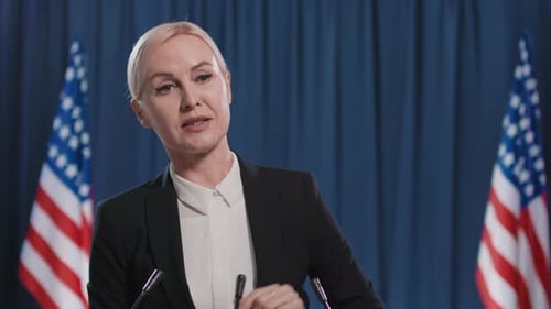 Confident Woman Speaking at Podium with Flags