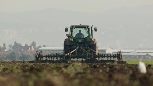 Tractor cultivating a green field in slow motion.