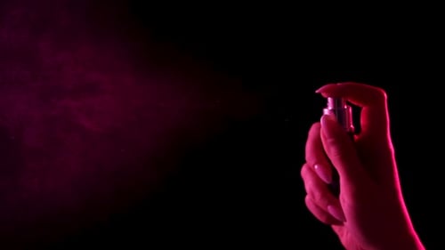 Hand Sprays Perfume with Pink Lighting on Black