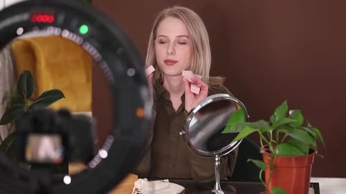 Hermosa mujer de cabello rubio maquillándose en cámara para un vlog en casa