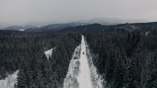 Aerial View From Drone on Car Driving Through Winter Snow Covered Forest