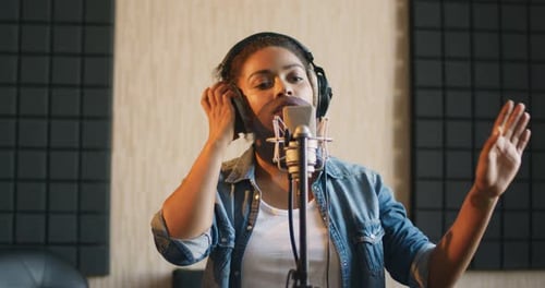 Professioneller Gesang. Junge schwarze Frau mit Kopfhörern singt vor dem Mikrofon im Sound Record Studio