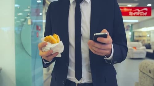 Businessman with Burger and Phone Walking in Mall
