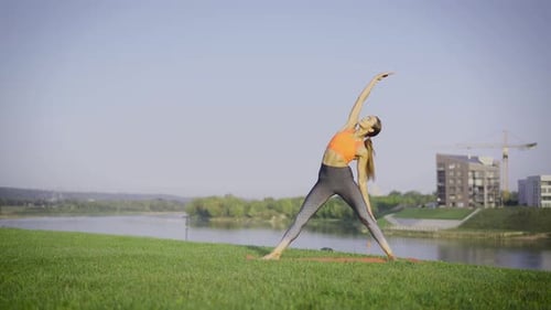 Woman Doing Yoga by River in City Park