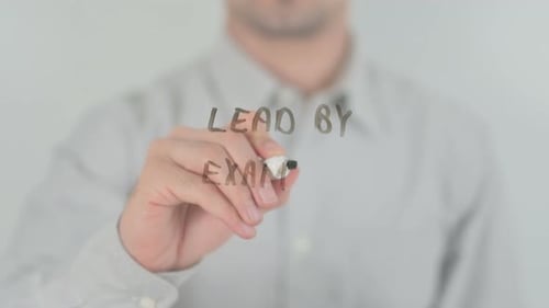 Man Writing "Lead By Example" on Glass Board