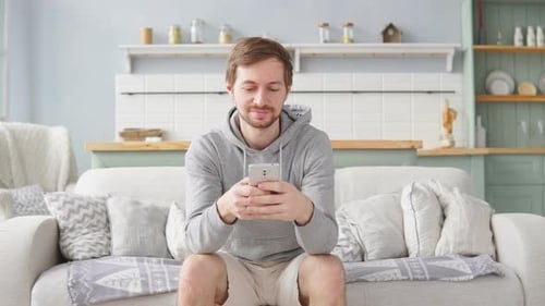 Young Adult Using Smartphone on Couch at Home