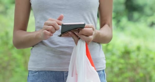 Ama de casa usando el teléfono móvil y sosteniendo bolsas de plástico en el parque