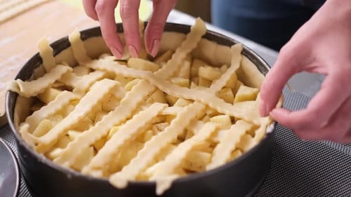 Hands Adding Dough Strips to Apple Pie