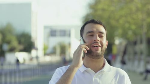 Smiling Young Man Walking on Street and Talking on Phone