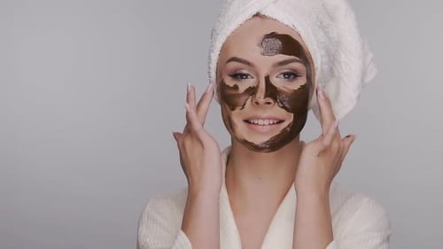 Woman Smoothes Clay Mask in Bath Robe and Head Towel