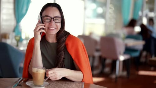 Charming Female Visitor of Cafe Brunette Woman is Calling By Phone and Smiling to Camera