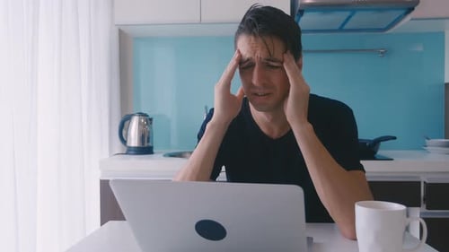 Worried Man Using Laptop in Bright Kitchen