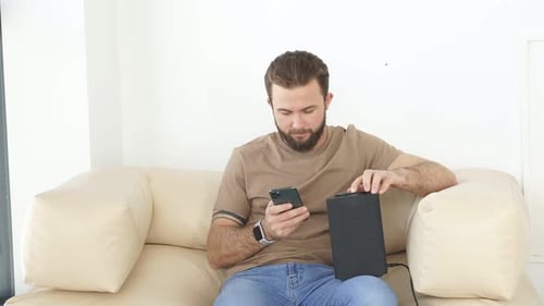 Man Connects Phone to Smart Speaker on Couch