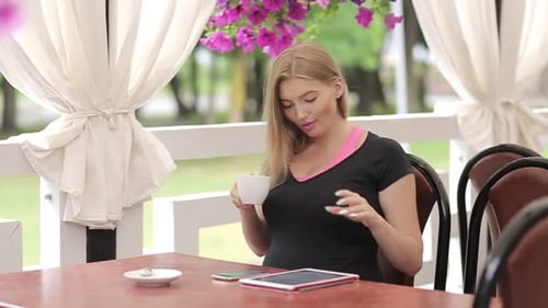 Beautiful girl with light hair wearing colorful shirt sitting in cafe with tablet