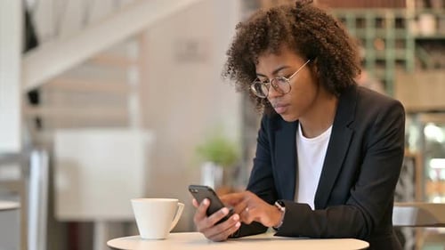 Serious African Businesswoman Using Smartphone at Cafe